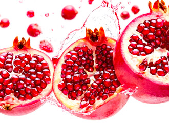 A dynamic display of ripe pomegranate pieces and droplets of juice and water, suspended in mid-air against a pristine white background. 
