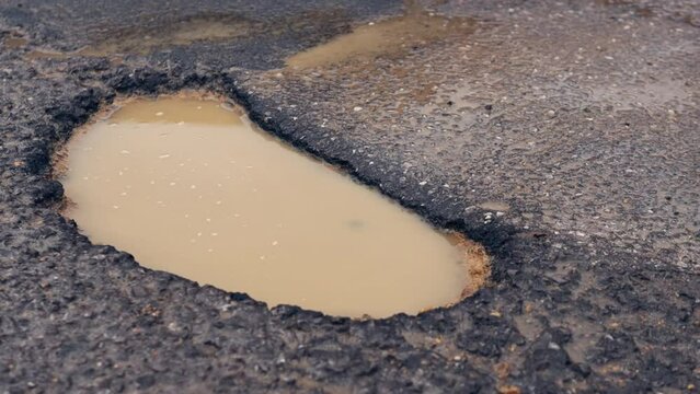 A large pothole in the middle of a crumbling road in the countryside. Close-up of a hole on the road during the rain.
