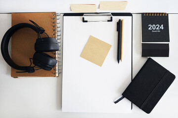 Clip folder with paper next to notepads, calendar, stickers, pens and black headphones on white...