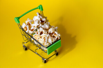 Freshly made popcorn on yellow background in a shopping cart