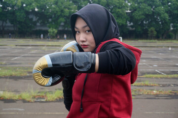 Young muslim girl in hijab and boxing gloves, training Muay Thai at gym park