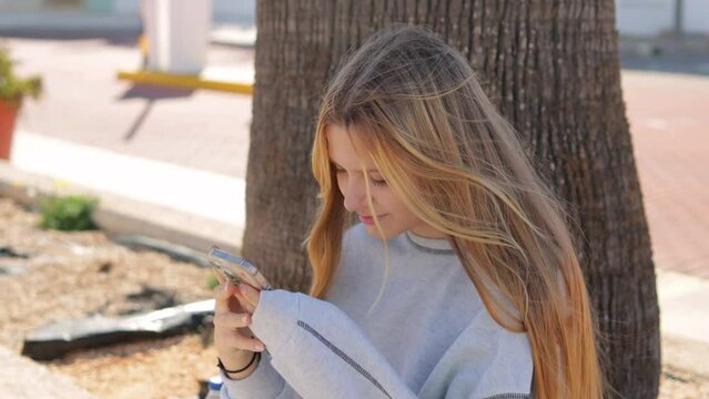 A teenage girl sits in the park and holds a phone in her hands. A teenager runs his finger across the phone screen. Concept of generation alpha, generation Z, diversity.