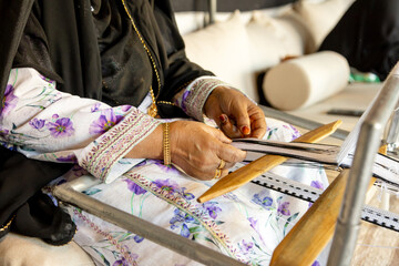 Senior Emirati woman using traditional weaving machine, hands in frame