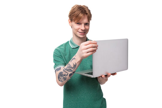 young positive red-haired caucasian guy in a green t-shirt works as an IT specialist and owns a laptop