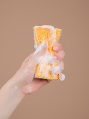yellow sponge with foam in hands on a beige background