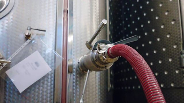 Red pipe attached to the hole in steel tank for high quality wine filtration, necessary equipment for wine fermentation, distillation and storage, taps and regulators on metal barrel for wright