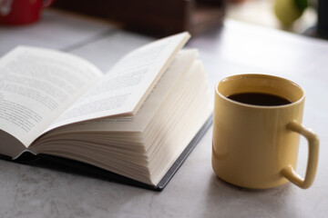 Open book with black cover and yellow cup of coffee on the table. Close up view.