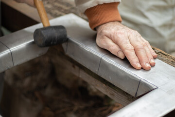 Close up view of man's hands with black rubber hammer that is making a frame out of galvanized steel