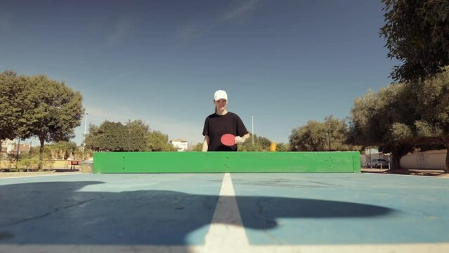 Table tennis outdoors. A girl in sportswear plays ping-pong with table tennis rackets in the summer in the park, active recreation