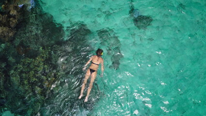 Slim girl snorkel crystal coral reef top down view. Slim sexy female in black bikini swim explore...