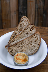 Three slices of wholemeal bread and hummus in a white bowl on the wooden table. 