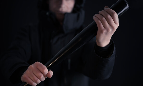 Male hooligan threatening in the dark with a baseball bat in his hands