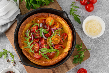 Savory cheese Dutch baby pancake. Dutch Baby pancake with mix tomatoes, parsley and arugula in cast iron pan on a concrete background. Delicious healthy breakfast.