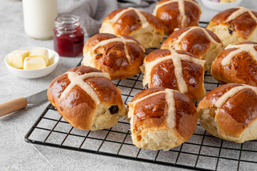 Freshly baked Easter hot cross buns with butter, berry jam and cup of tea on a gray concrete background. Delicious Easter breakfast. Top view.