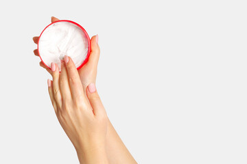 Women's hands hold a jar of cream and apply it to their hands. On a light background.