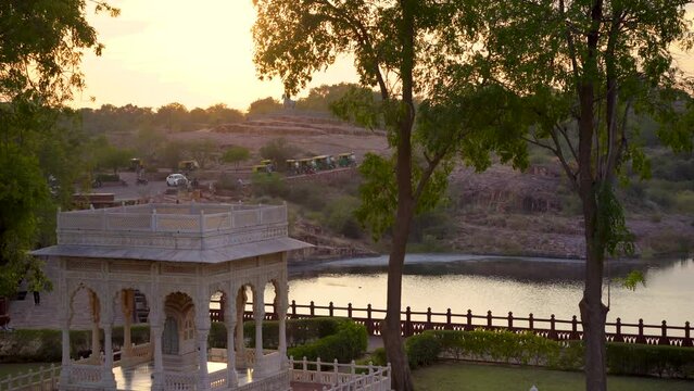 Panning shot showing lake bordered by trees at sunset going to marble arches in the landmark mausoleum jaswant thada near mehrangarh fort Jodhpur
