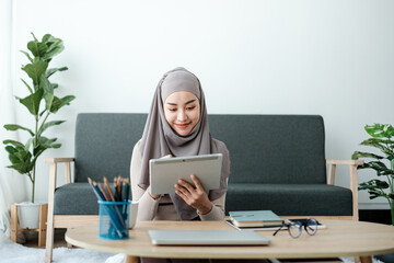 Young business Asian Business muslim woman in hijab using a tablet, Sitting near the window in the living room. 