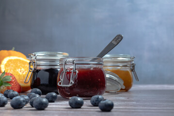 Homemade strawberries marmalade, assortment of homemade jams in glass jars. Front view, seasonal fruit jam, oranges, strawberries and blueberries.