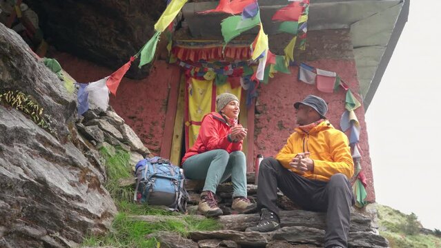 Backpackers Couple at Small Buddhist monastery decorated multicolored Tibetan prayer flags with mantras on climbing Mera peak route in Makalu Barun National Park. Peaceful and sacred place 4K video