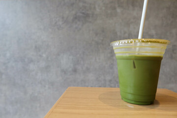 close up of green tea matcha lattee coffee drank a few slip with straw and on a wooden table with grey wall background