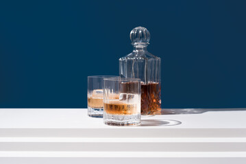 Dos vasos de whisky con hielo y decantador sobre fondo azul	