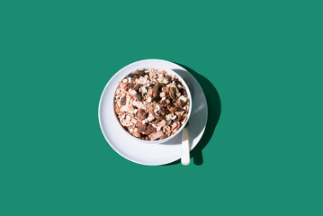 Cereal de granola muesli en un tazón blanco con cuchara sobre fondo verde. Vista superior