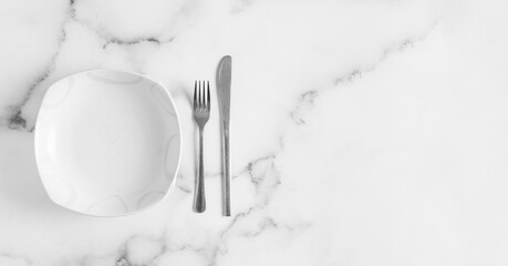 Empty plate witha fork and knife on white table top view