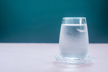 A glass of water with ice on pink table.