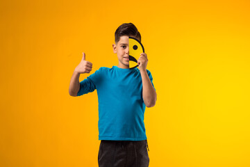 Child boy holds emoticons with  sad emotions on half face and showing thumb up gesture.