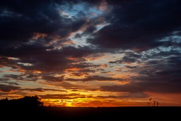 Sunset in the summer field. The clouds in the sky are lit by the setting sun on the horizon. The blue sky changes color in the rays of the sun at sunset. Clouds in the sky above the horizon.