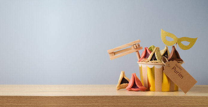 Jewish holiday Purim concept with colorful hamantaschen cookies and carnival mask on wooden table over gray background