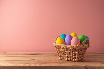 Easter holiday concept  with easter eggs in basket on wooden table over pink background