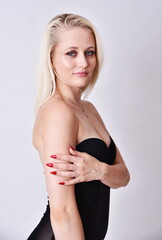 Fototapeta premium Blond caucasian woman, bright skin and blue eyes. Model in her 20's. Woman wearing tight, black dress.