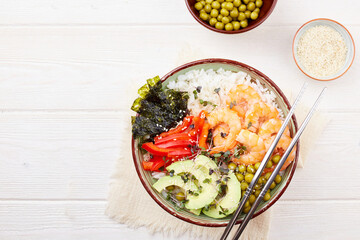 A poke bowl with shrimp, rice, avocado, pepper, green peas, nori and micro greens on a white wooden background. Hawaiian diet dish with seafood 