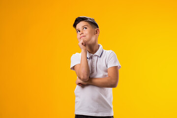 Thoughtful child boy holds chin on yellow background. Dreaming concept