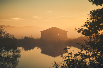 Old barn on lake shore on misty sunrise. High quality photo - 744685551