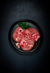 raw steak, calf's neck on the bone, fresh meat, on a black plate, top view, no people,
