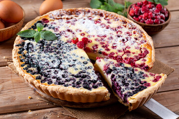 Homemade raspberry pie with short pastry, ripe raspberries and blueberries cut into pieces on a wooden table.