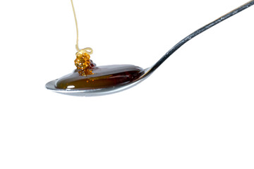 Honey flows onto an almost full teaspoon. Isolated on transparent background