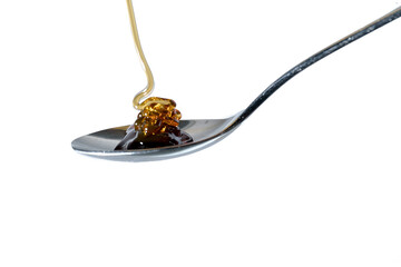 Honey flows onto a teaspoon. Isolated on transparent background