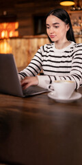 Woman using laptop and drinking coffee in cafe working online freelance. Copy space