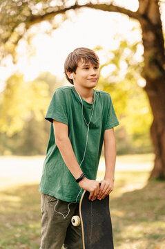 Vertical image of teenager boy holding skateboard and listening music at headphones...