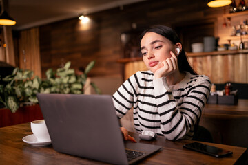 Fototapeta premium young pleased happy businesswoman sit in cafe using laptop computer listening music with earphones.