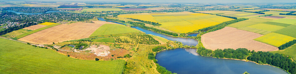 Fototapeta na wymiar Sunny day in the countryside. Rural landscape in daylight. Aerial view of a meandering river and cultivated fields. Horizontal banner