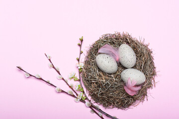 Nest mit gepunkteten Ostereiern und Blütendekoration vor pinkem Hintergrund