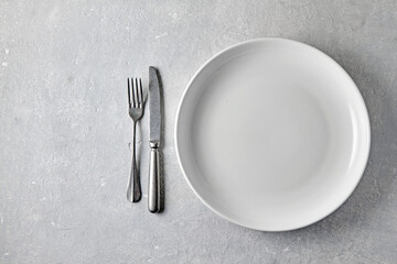 White ceramic plate with cutlery on a light stone table. Template for food, top view with copy space
