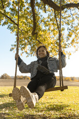 Adolescent woman swinging and smiling during sunset on a farm, wearing black pants, boots and a blue jacket