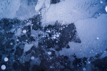 Top view of air bubbles and formations formed on the surface of frozen water. Blue background.
