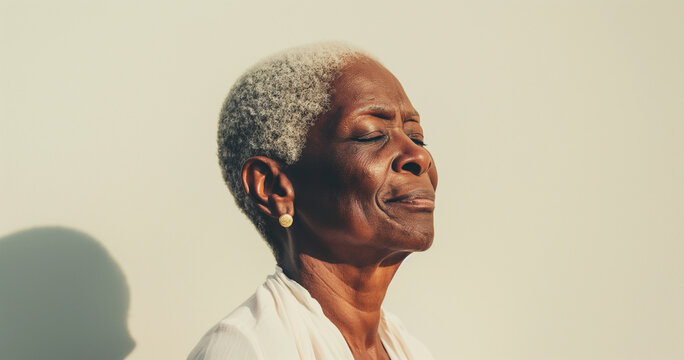 Close up portrait of mature black woman with short gray hair standing in sunlight, peaceful and contemplative expression