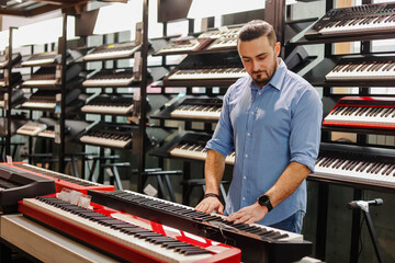 Young bearded man choosing electric piano or synthesizer in a musical shop. © glebcallfives